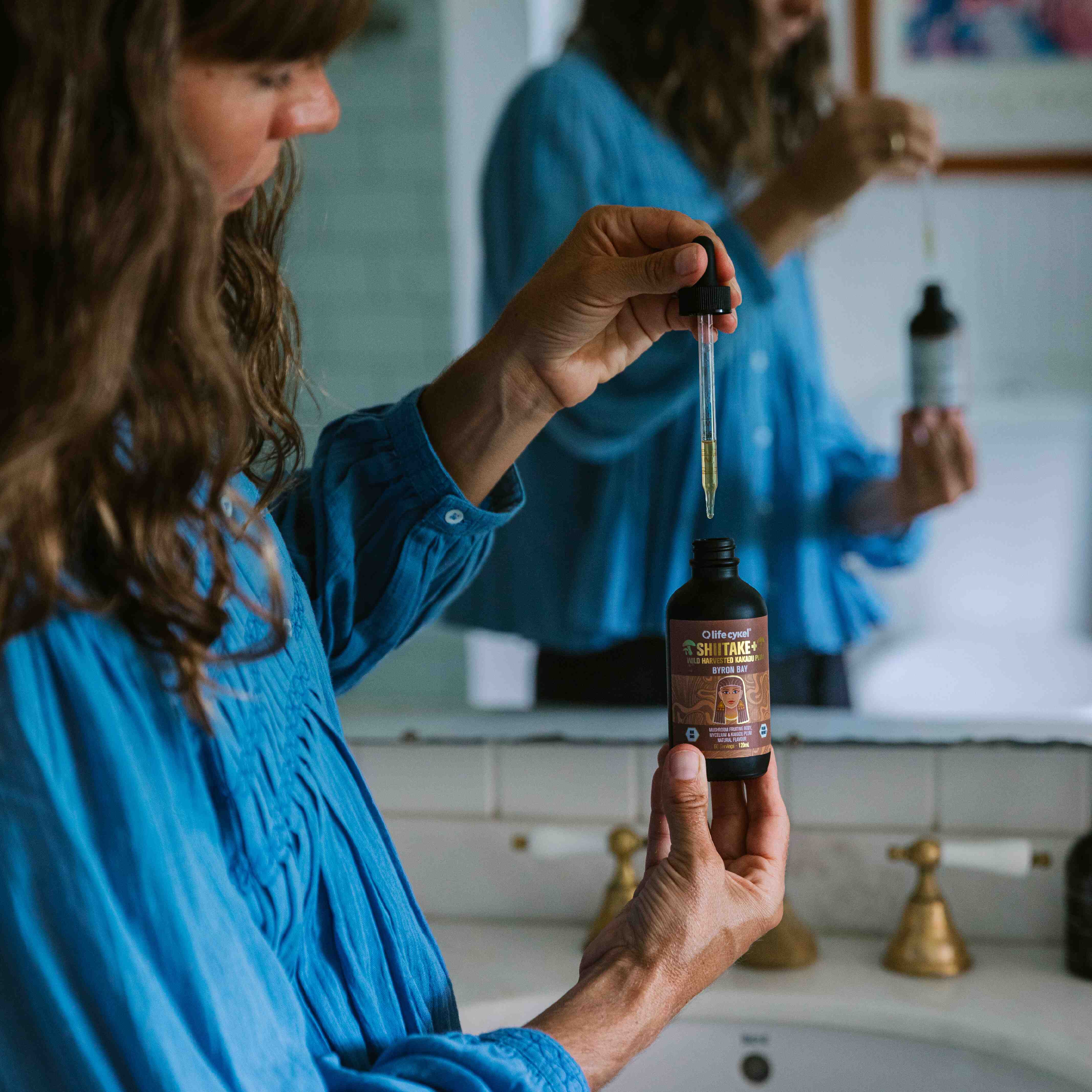 Woman in a bathroom holding a bottle of CBD oil with a dropper.