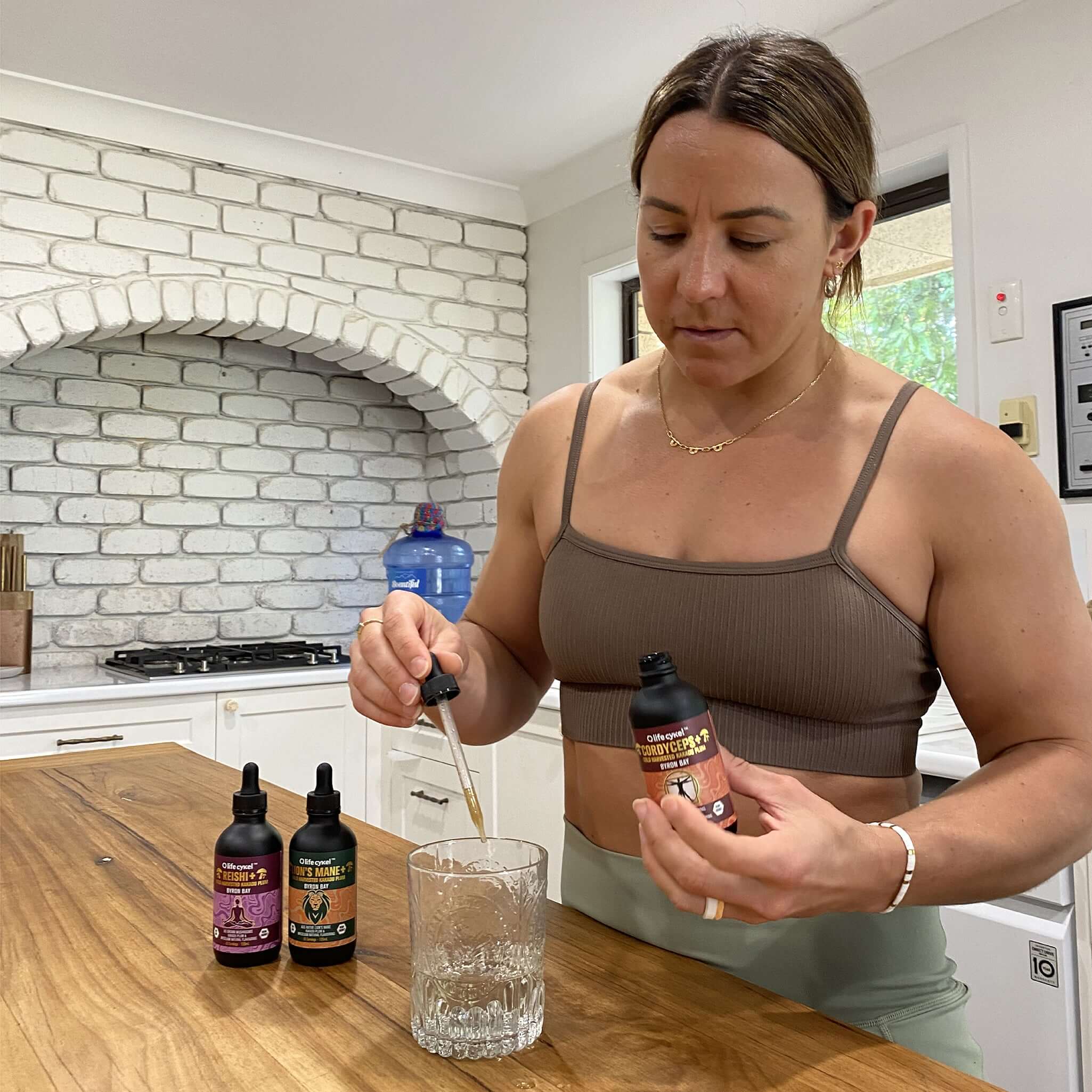 Woman pouring Lifecykel mushroom extracts  from a bottle into a glass in a kitchen.